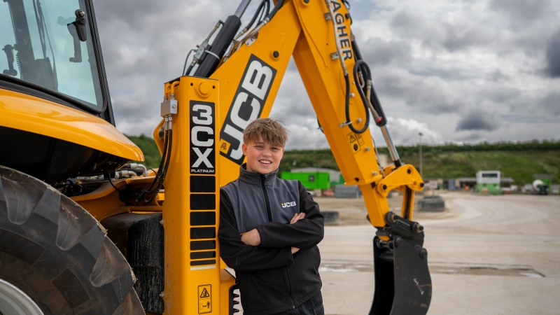 UK's youngest digger driver leans against JCB 3CX backhoe loader