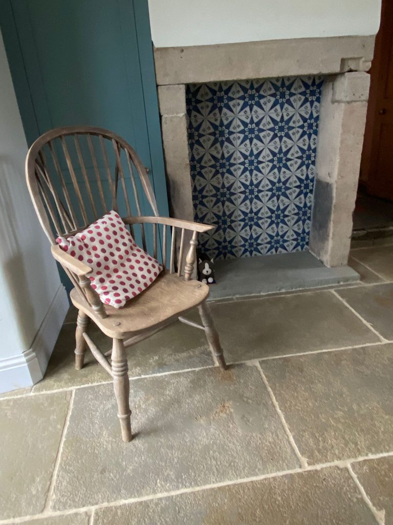 A natural stone tile floor in a room with a chair, toy cat and fireplace