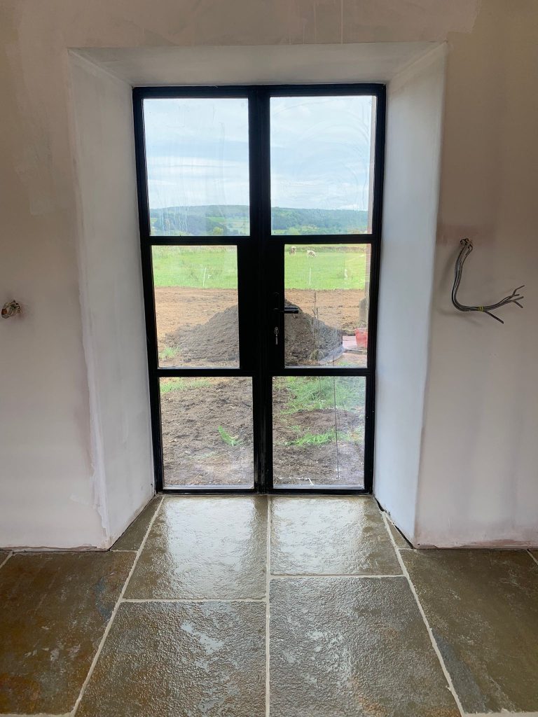 A natural stone tile floor with modern glass doors and a countryside view